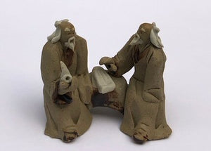 Ceramic Figurine<br>Two Mud Men Sitting On A Bench Holding Pipe<br>2"